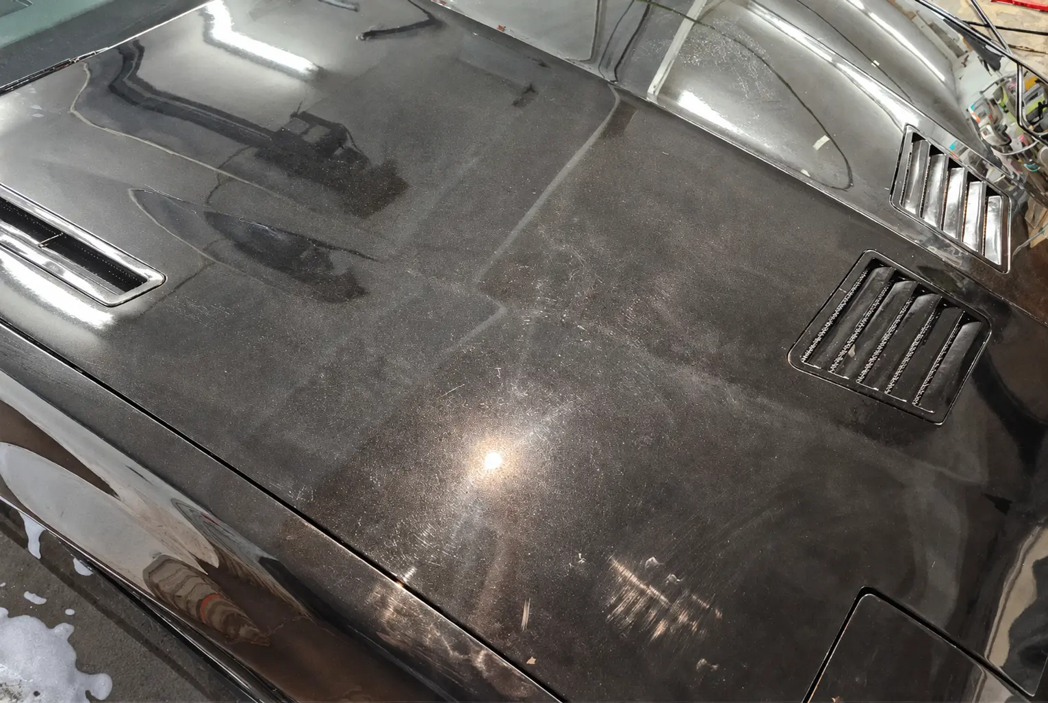 Vehicle hood before paint correction under inspection lighting