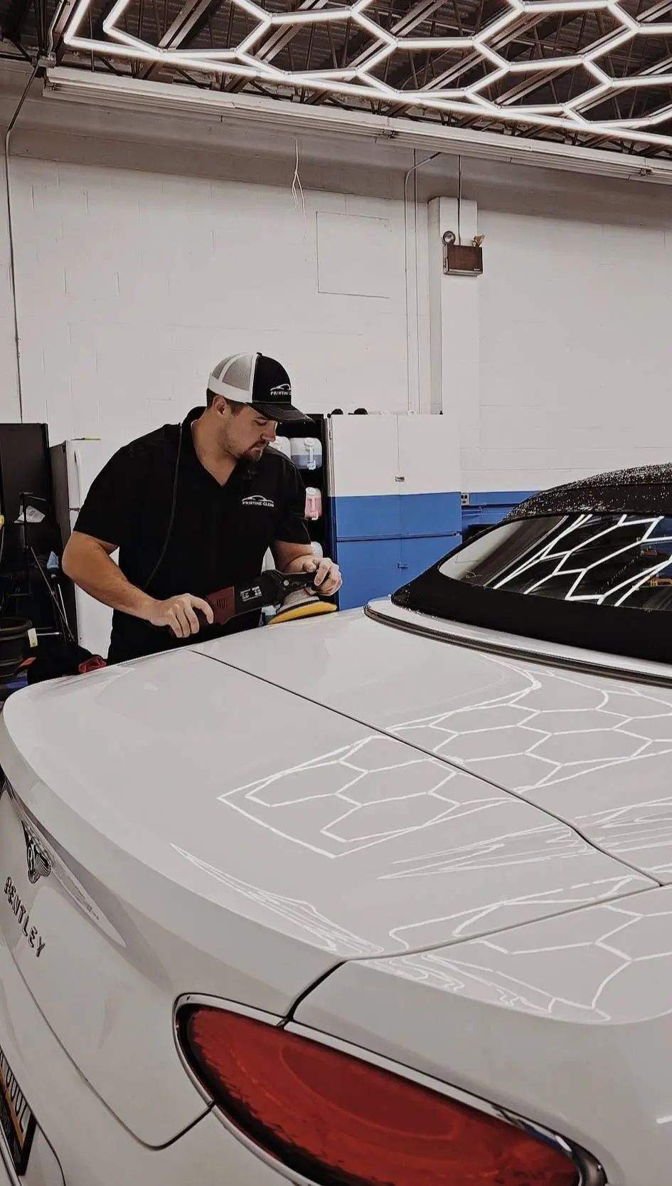 Owner machine polishing a white Bentley under inspection lighting