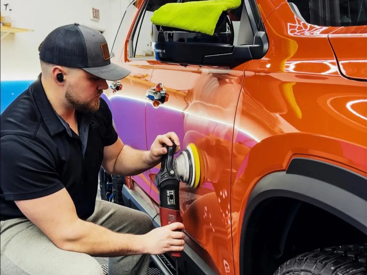 Pristine Clean technician polishing an orange Volkswagen before coating
