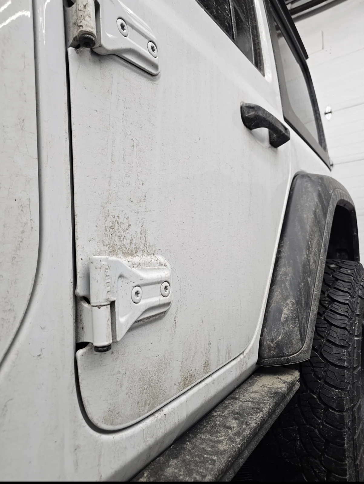 Heavy winter salt and grime around a white Jeep door, hinges and lower rocker